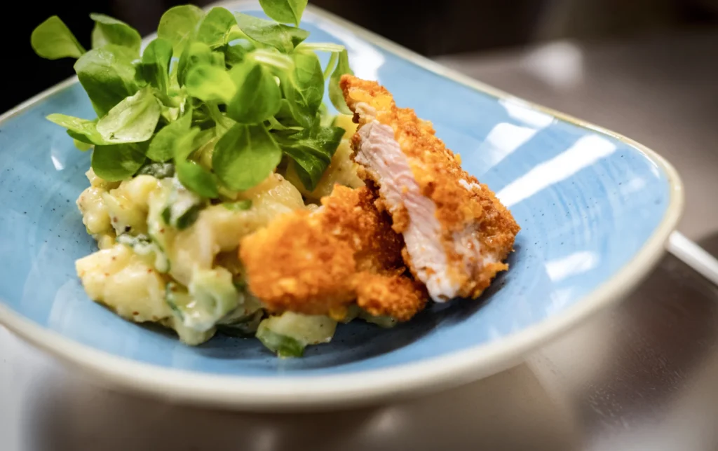 Kartoffelsalat, Schnitzel und Salat auf einem hellblauen Teller